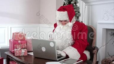 忙碌的圣诞老人用手提电脑和数码平板电脑准备礼物，整理他的信件，并收到一份来自